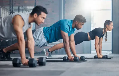 Group, workout and dumbbell push up at gym for muscle, power or strength. Teamwork, sports or energy of people, athletes or bodybuilder friends exercise or training at fitness center for healthcare